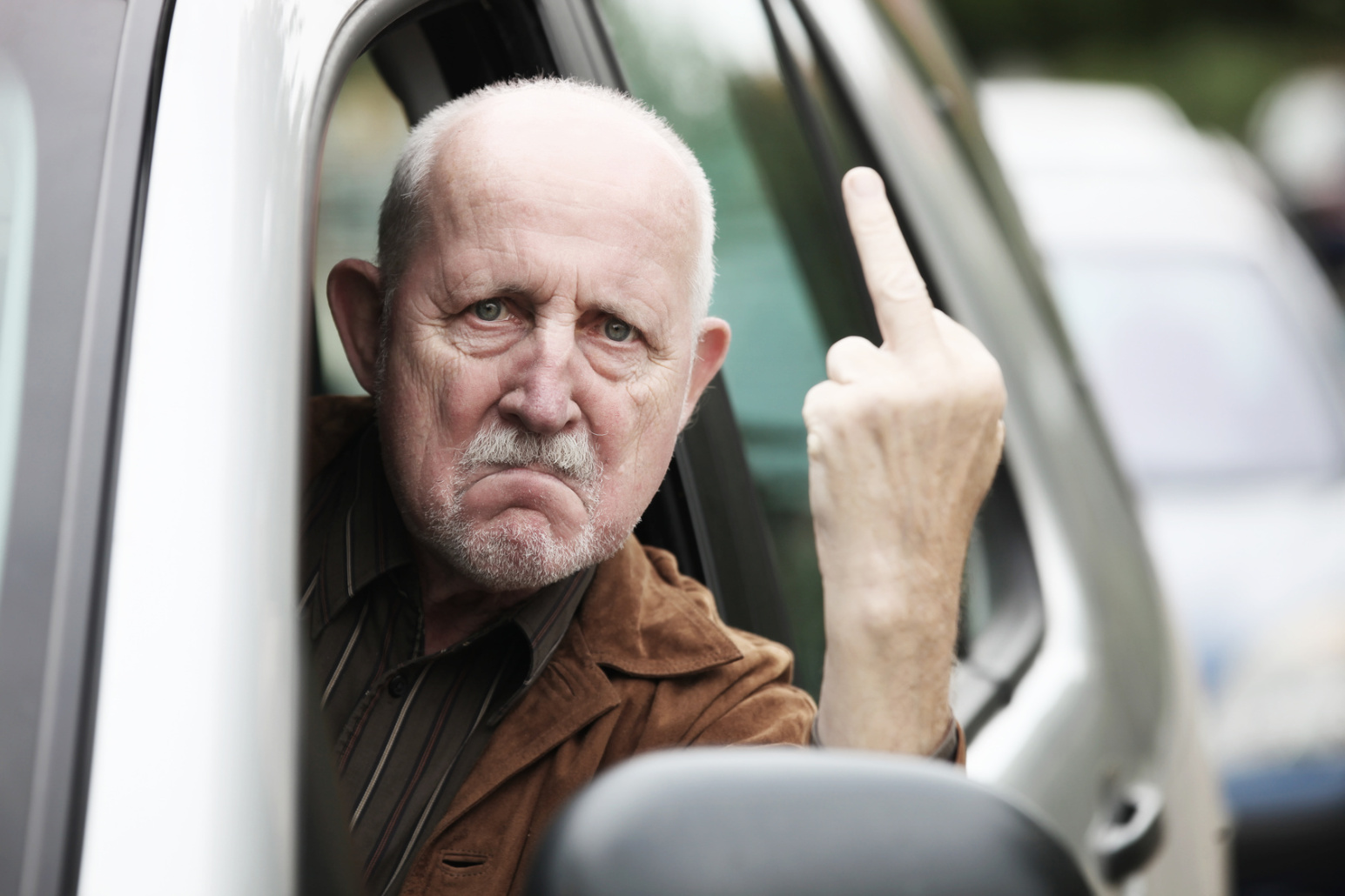 Älterer Mann sitzt im Auto, hält den Kopf aus dem Fenster und zeigt mit wütendem Gesichtsausdruck den Mittelfinger; Kurtz Detektei Düsseldorf, Halterermittlung, Kennzeichenermittlung, Detektiv Düsseldorf